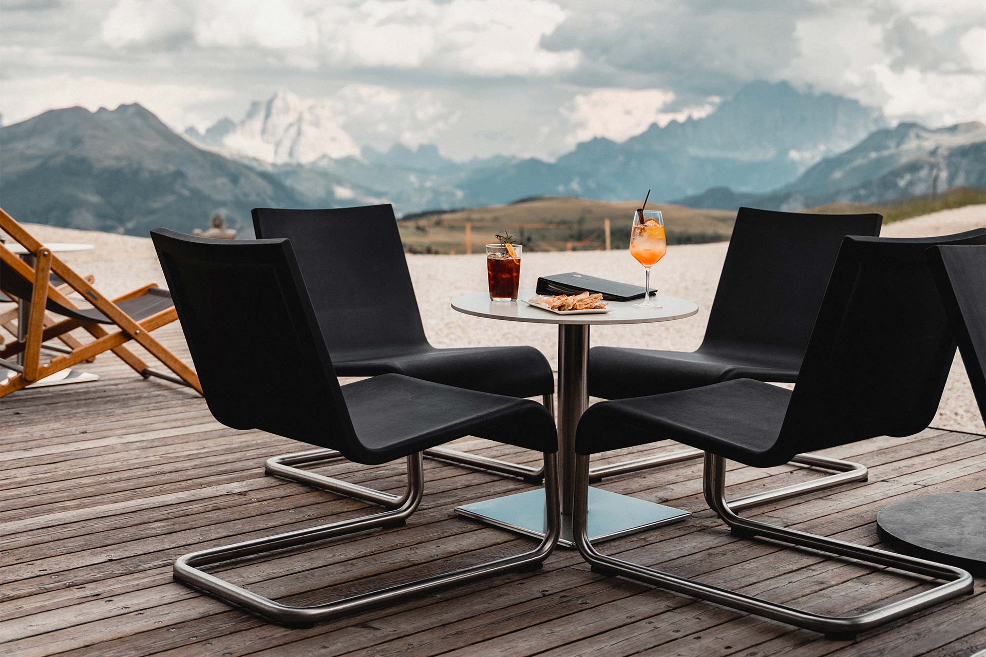 L'Alpine Lounge arredato con delle sedie, tavolini e divanetti, dal quali gli ospiti possono godere di una vista panoramica su Corvare. In mezzo una stufa per riscaldare l'ambiente.